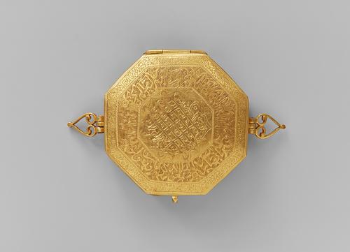 Top of Gold Qur’an case was worn as an arm ornament, decorated with engraved patterns. View of the palmette-shaped loops on either side of the box indicate how it originally would have been tied with a silk string around the bicep.